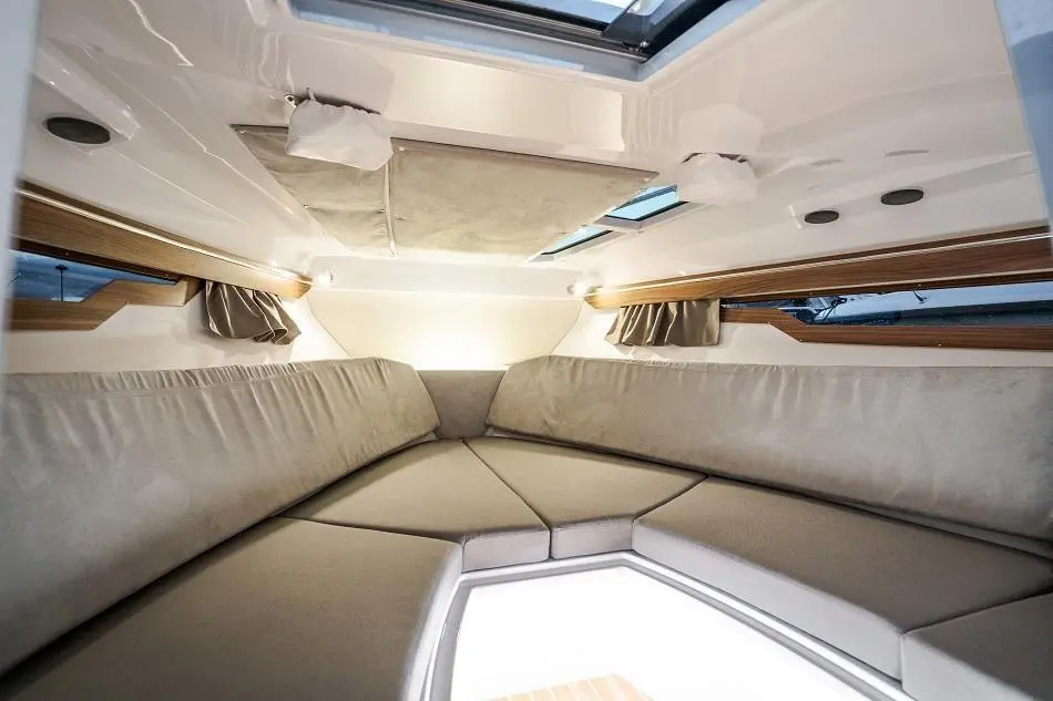 Interior of a modern boat cabin featuring grey seating, overhead lights, and small windows for natural light.